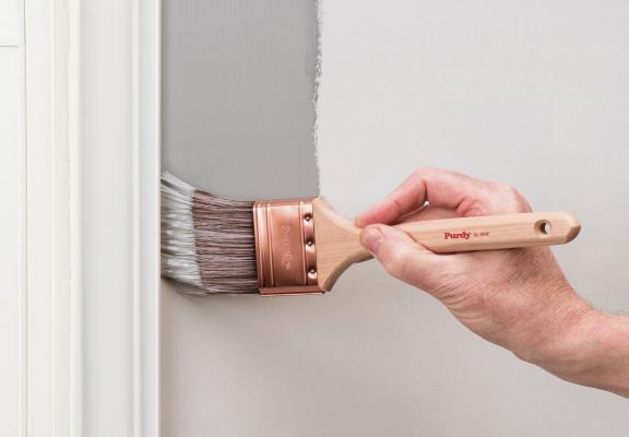 A hand using a brush to cut in gray paint neatly along white trim, no masking tape in sight