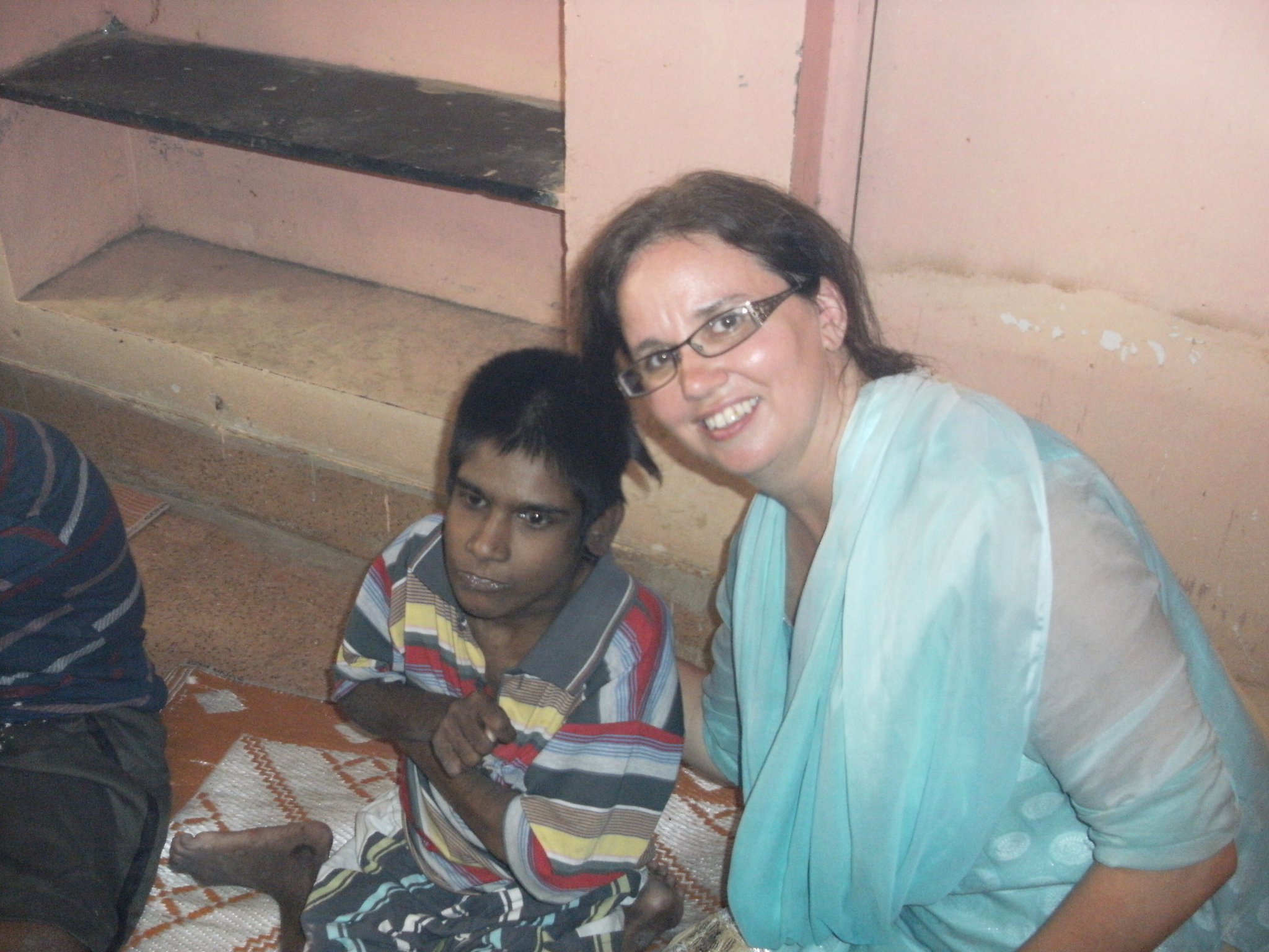 Anne Marie kneeling beside a smiling boy on a woven mat